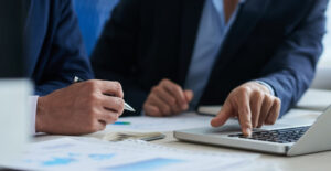 Checklist Fiscal Mensal: profissionais conferindo dados no notebook e documentos, representando rotina fiscal e organização mensal.